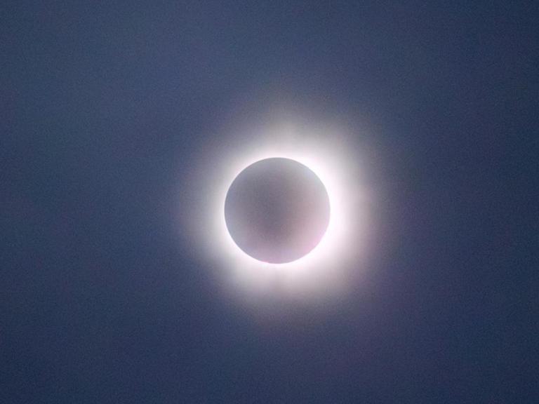 The image captures a solar eclipse in its totality phase, 月亮完全遮住太阳的地方, leaving only the bright corona visible as a glowing ring around the darkened disk. The sky appears dark, adding to the dramatic effect of the eclipse. 软, glowing light of the corona creates a striking contrast against the shadowed moon, making this a captivating depiction of a natural celestial event.